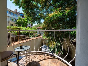 Un balcon avec une table ronde et des chaises, une vue sur des immeubles et un arbre aux feuilles vertes.