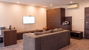 Una sala de estar moderna con un sofá gris, un televisor de pantalla plana, un mueble de madera y un escritorio pequeño con una computadora portátil.