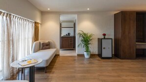 A modern living room with a sofa, a small table, a potted plant, a cabinet, and a kitchenette in the background. - Clarks Inn Suites Hyderabad (Hyderabad)