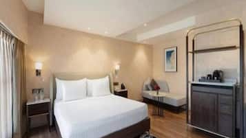 A hotel room with a bed, bedside tables, a sofa, a small table, and a kitchenette area.