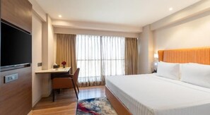 A hotel room with a bed, a desk, a chair, a television, and a window with curtains. - Clarks Inn Suites Hyderabad (Hyderabad)