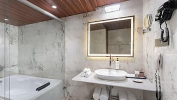 A modern bathroom with a marble wall, a large mirror, a sink, a bathtub, and a telephone.