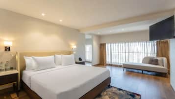 A hotel room with a large bed, bedside tables, a sofa, a TV, and a window with curtains.