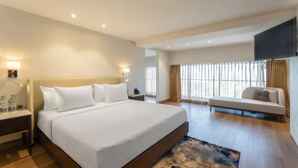 A hotel room with a large bed, bedside tables, a sofa, a TV, and a window with curtains. - Clarks Inn Suites Hyderabad (Hyderabad)