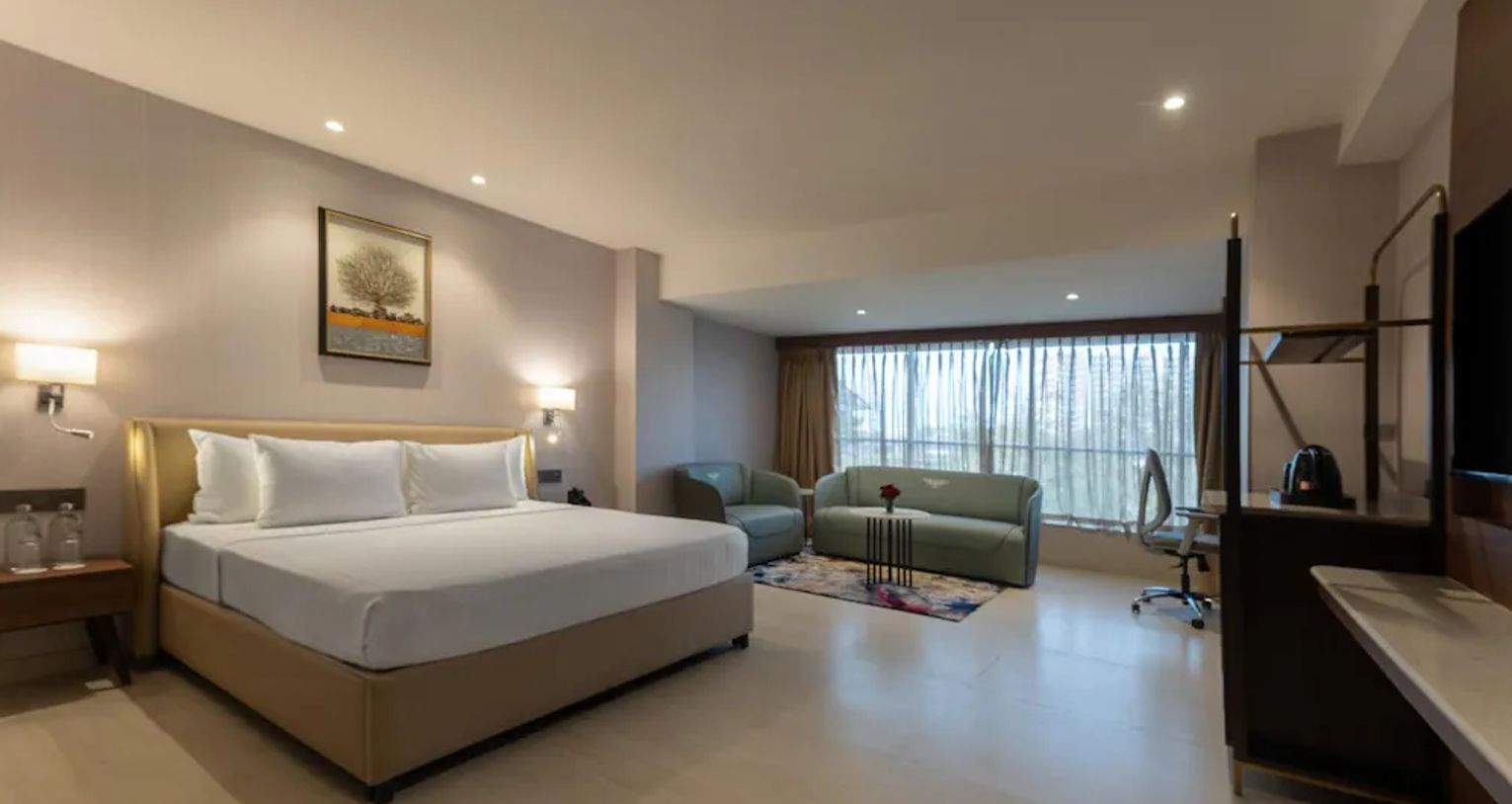 A hotel room with a bed, a desk, a chair, a sofa, and a TV.