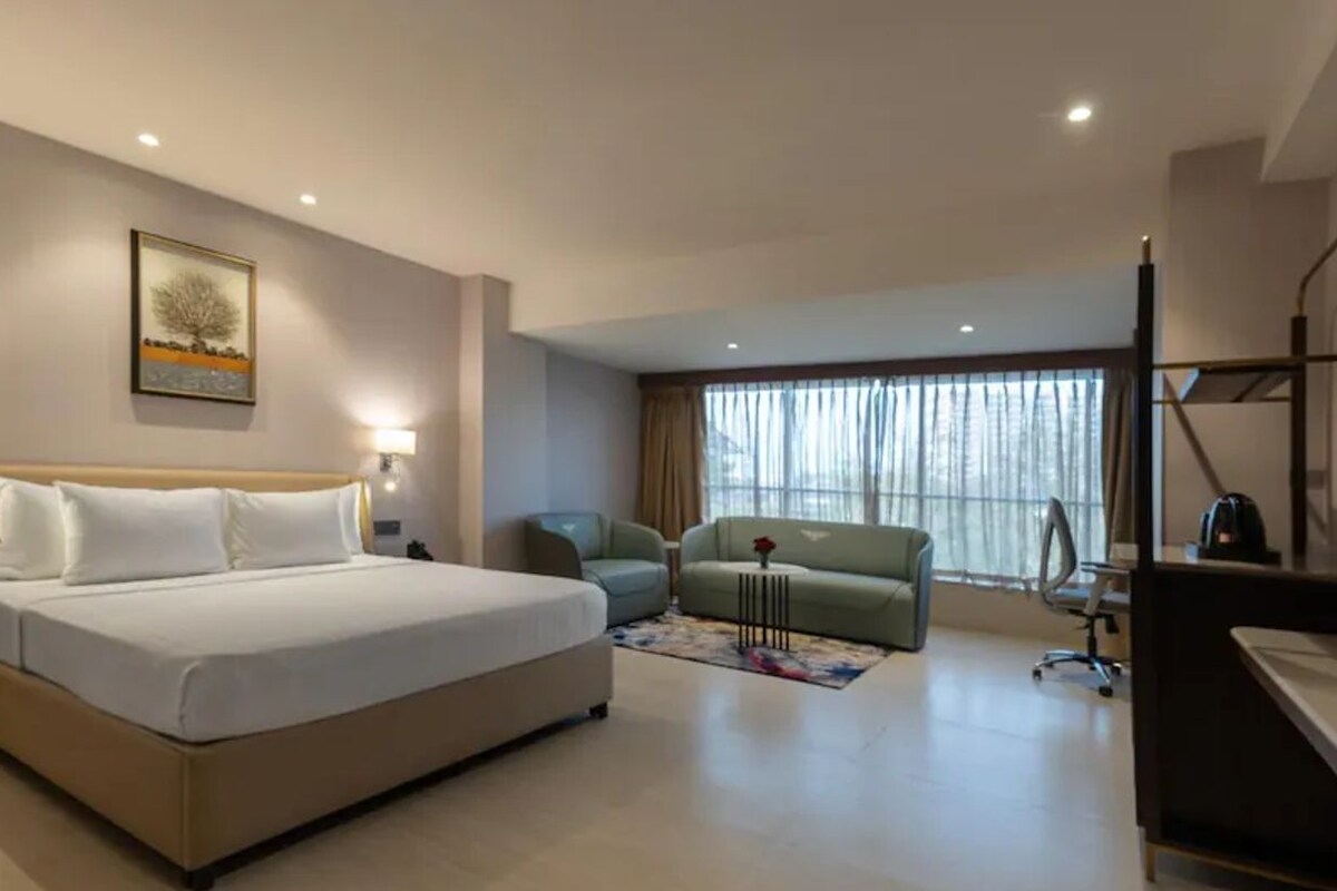 Ein Hotelzimmer mit Bett, Schreibtisch, Sessel, Sofa und Fernseher.