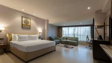 A hotel room with a bed, a desk, a chair, a sofa, and a TV.