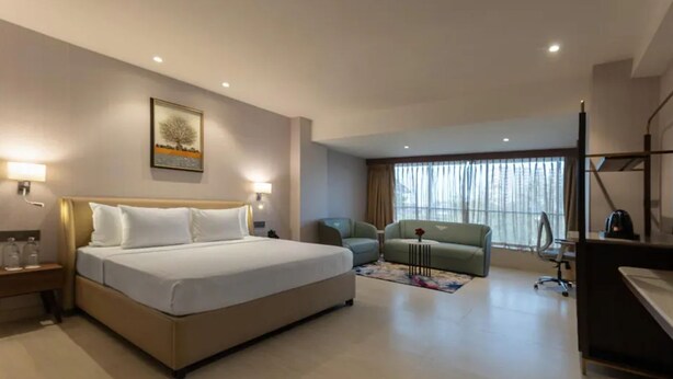 Ein Hotelzimmer mit Bett, Schreibtisch, Sessel, Sofa und Fernseher.