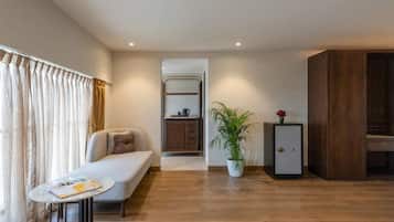 A modern living room with a sofa, a small table, a potted plant, a cabinet, and a kitchenette in the background.