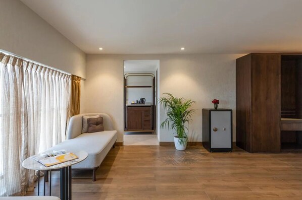 A modern living room with a sofa, a small table, a potted plant, a cabinet, and a kitchenette in the background. - Clarks Inn Suites Hyderabad (Hyderabad)