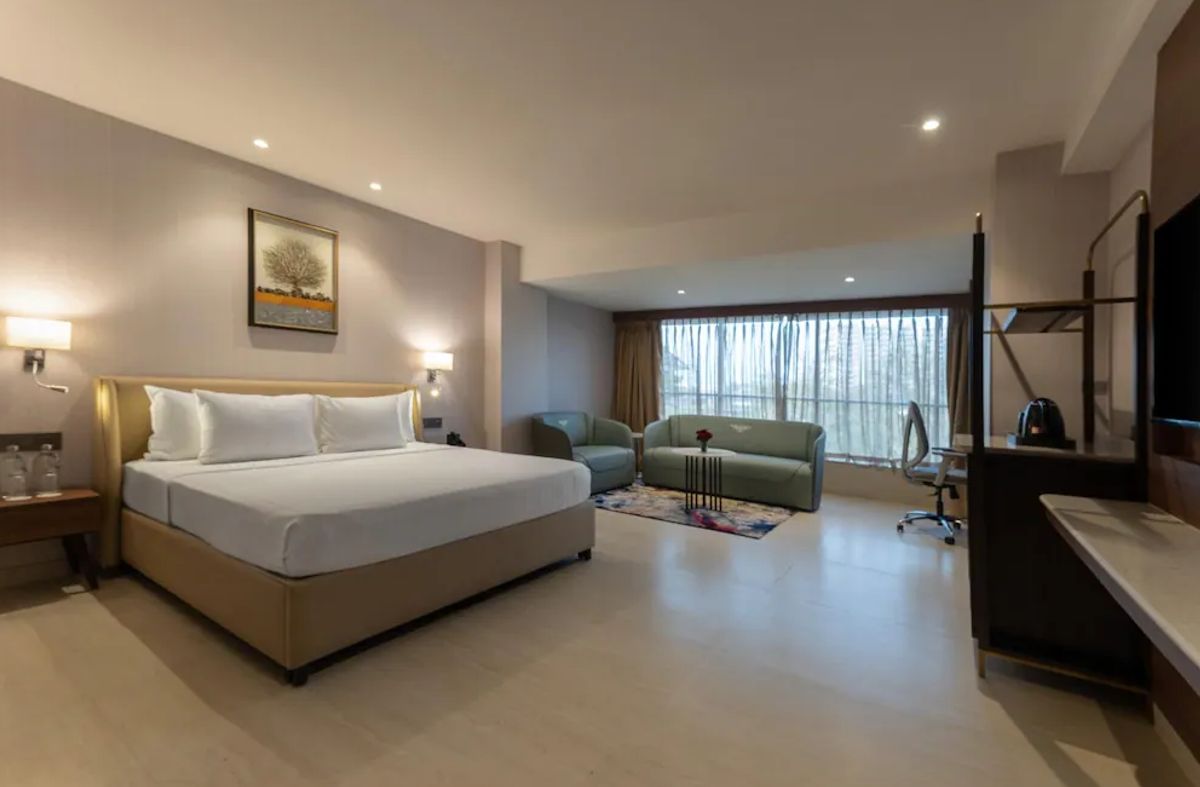 A hotel room with a bed, a desk, a chair, a TV, and a window with curtains.