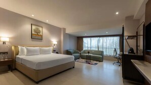 Ein Hotelzimmer mit Bett, Schreibtisch, Stuhl, Fernseher und einem Fenster mit Vorhängen.