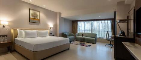 A hotel room with a bed, a desk, a chair, a TV, and a window with curtains.