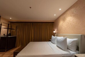Een hotelkamer met een bed, bureau, stoel en gordijn.