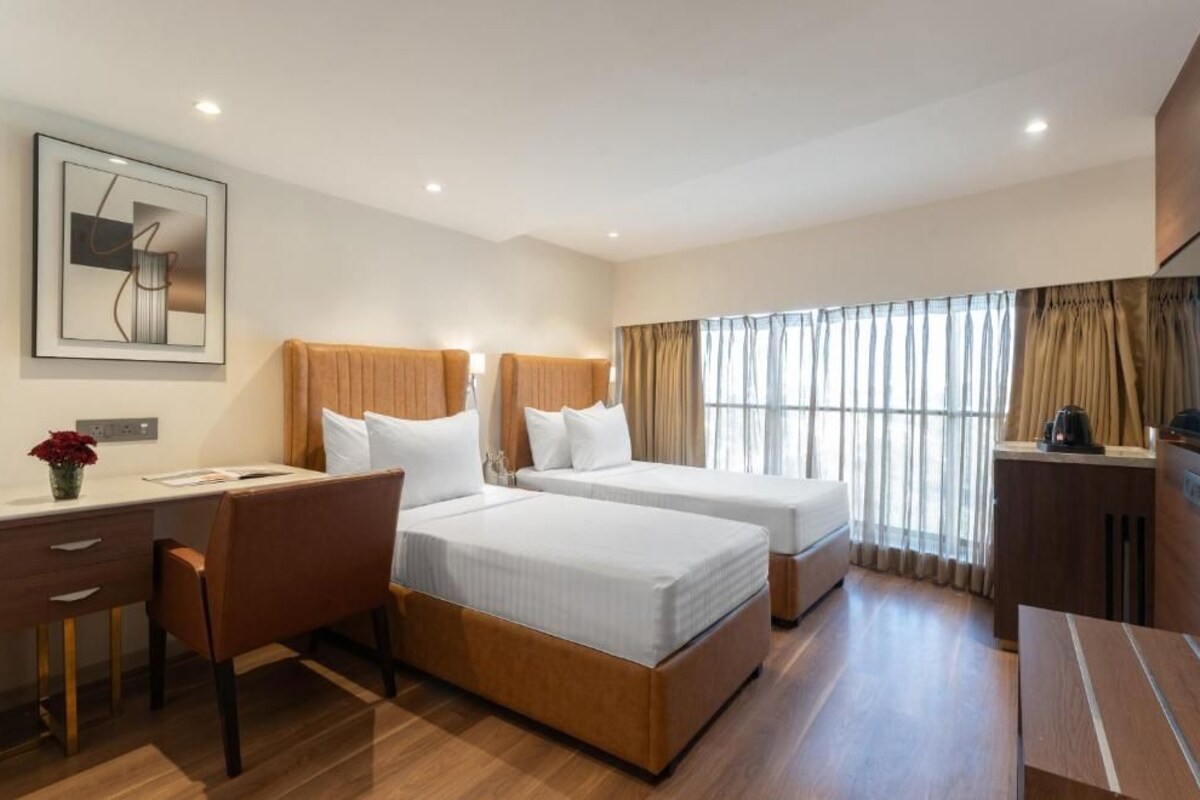 Ein Hotelzimmer mit zwei Betten, einem Schreibtisch, einem Stuhl, einem Fernseher und einem fenster mit Vorhängen.