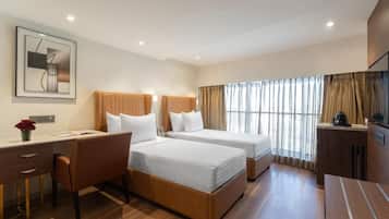 A hotel room with two beds, a desk, a chair, a TV, and a window with curtains.