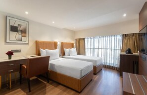 A hotel room with two beds, a desk, a chair, a TV, and a window with curtains. - Clarks Inn Suites Hyderabad (Hyderabad)