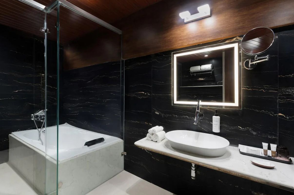A modern bathroom with a glass-enclosed shower, a freestanding bathtub, a marble wall, a large mirror, and a white sink.