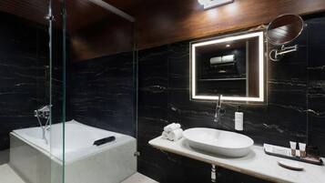 A modern bathroom with a glass-enclosed shower, a freestanding bathtub, a marble wall, a large mirror, and a white sink.