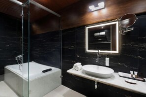 Een moderne badkamer met een glazen douchecabine, een vrijstaand bad, een marmeren wand, een grote spiegel en een witte wastafel.