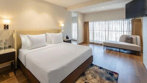 A hotel room with a large bed, bedside tables, a sofa, a TV, and a window with curtains. - Clarks Inn Suites Hyderabad (Hyderabad)