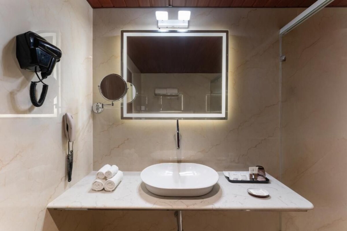 Een badkamer met een rond wastafel, een spiegel, een haardroger en een handdoekhouder.