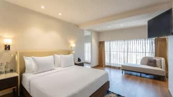 A hotel room with a large bed, bedside tables, a sofa, a TV, and a window with curtains.