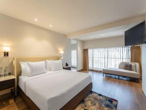 Ein Hotelzimmer mit einem großen Bett, Nachttischen, einem Sofa, einem Fernseher und einem Fenster mit Vorhängen.