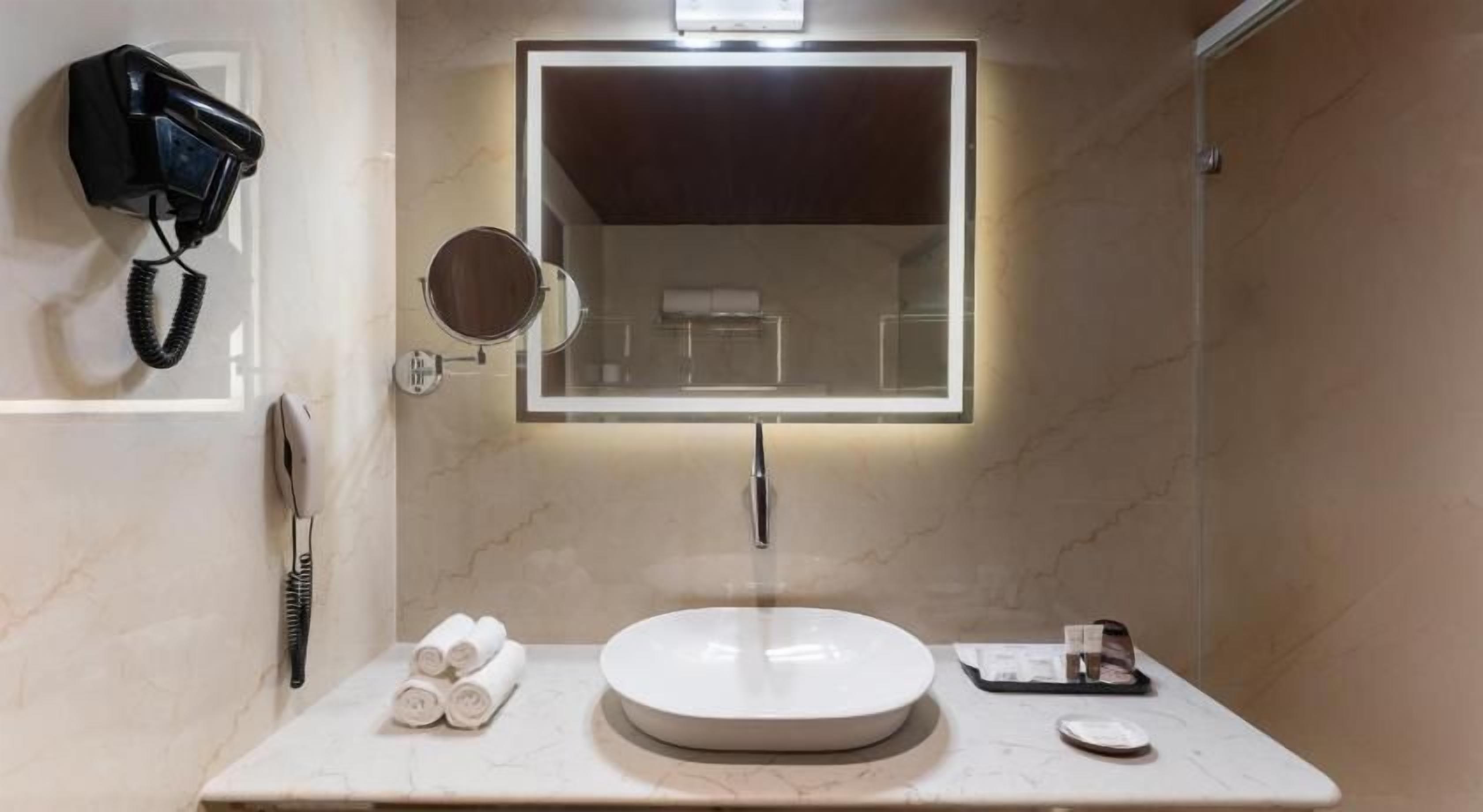 A bathroom with a round sink, a mirror with a light, a hairdryer, and towels on the counter.