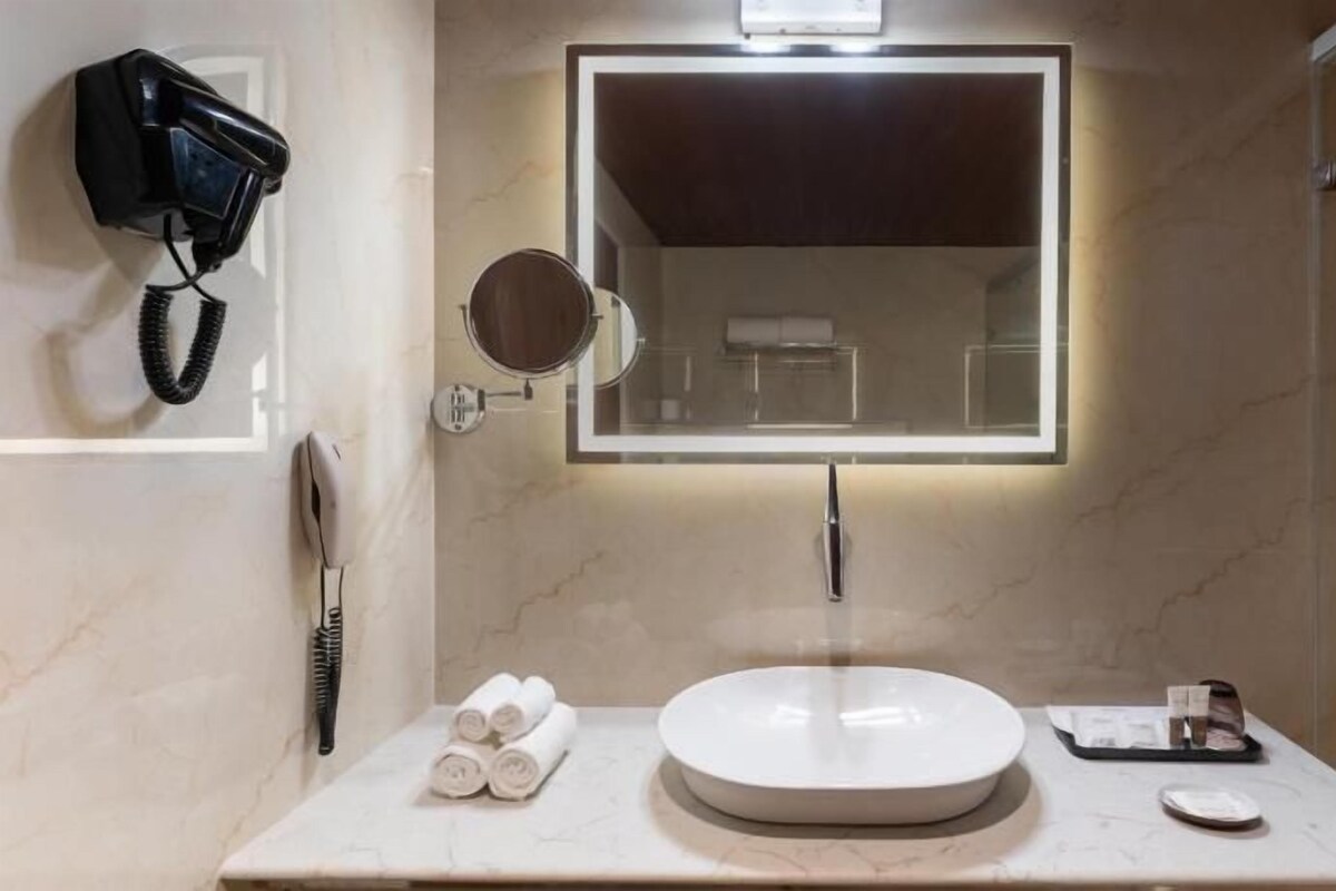 Een badkamer met een rond wastafel, een spiegel met verlichting, een haardroger en handdoeken op het aanrecht.
