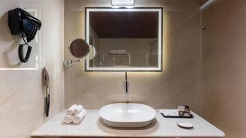 A bathroom with a round sink, a mirror with a light, a hairdryer, and towels on the counter.