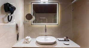 A bathroom with a round sink, a mirror with a light, a hairdryer, and towels on the counter. - Clarks Inn Suites Hyderabad (Hyderabad)