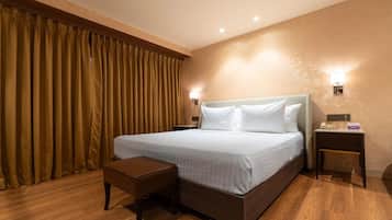 A hotel room with a large bed, a bedside table, a nightstand, a wooden bench, and a wall-mounted lamp.