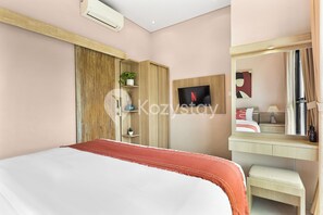 A modern hotel room with a bed, a wooden wardrobe, a small desk with a mirror, and a TV mounted on the wall. - Surio Villa by Kozystay - Nusa Dua (Kutuh)