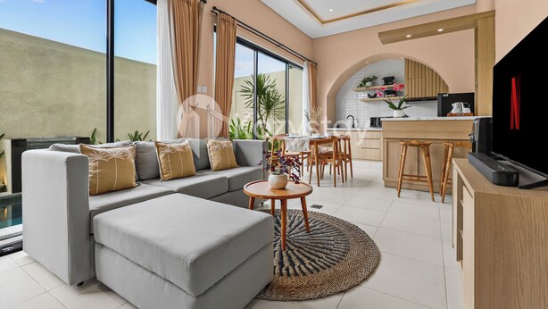 Ein modernes Wohnzimmer mit grauem Sofa, einem runden Couchtisch und einer Küchenzeile mit Fernseher, Holzbarhocker und Esstisch.