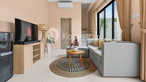Ein modernes Wohnzimmer mit Flachbildfernseher, einer Couch, einem Couchtisch und einem großen Fenster mit Vorhängen.