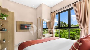 Ein Schlafzimmer mit einem großen Bett, einem an der Wand montierten Fernseher, einem Fenster mit Vorhängen und Blick ins Grüne.