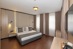 A modern hotel room with a large bed, wooden flooring, a desk with a lamp, and a large window with curtains. - Taksim YEZ Hotel (Istanbul)