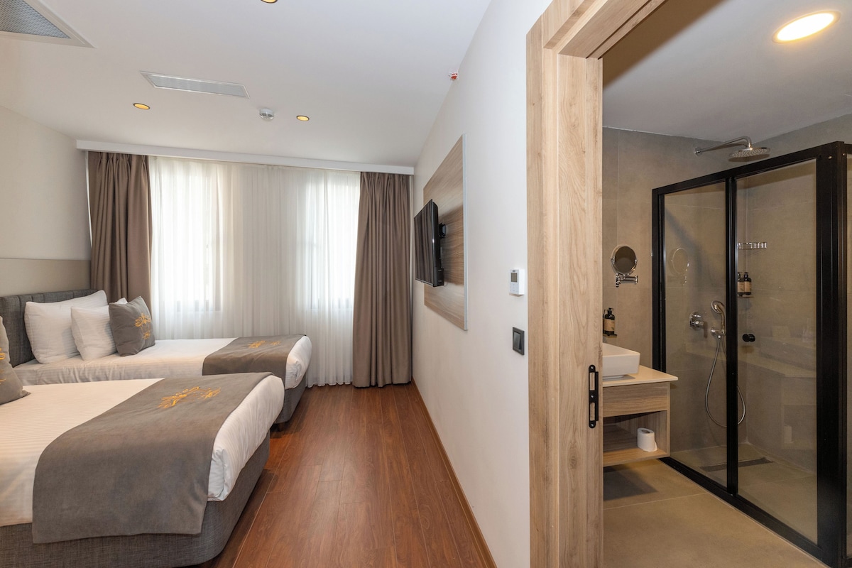 A hotel room with two beds, a shower area, and a TV mounted on the wall.