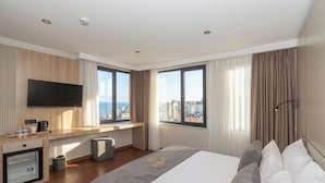 A modern hotel room with a large bed, a flat-screen TV mounted on the wall, a small kitchenette, and a city view through large windows. - Taksim YEZ Hotel (Istanbul)