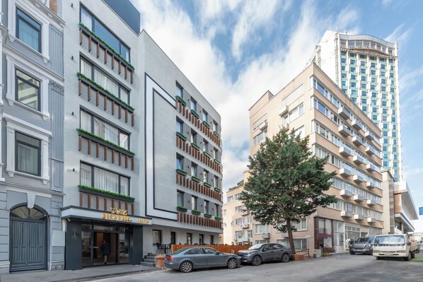 A hotel with a modern facade, multiple balconies with greenery, and a parking area with cars. - Taksim YEZ Hotel (Istanbul)