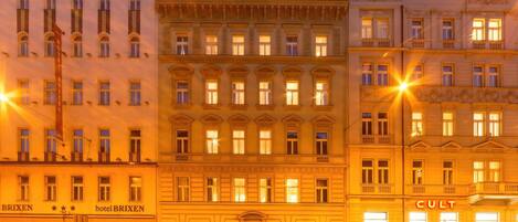 Una hilera de edificios históricos con ventanas iluminadas y carteles que indican 'hotel BRIKEN' y 'CULT'.