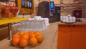 A kitchen area with a fruit bowl, a tray of oranges, a coffee machine, and a display of mugs. - Hotel S42 (Prague)