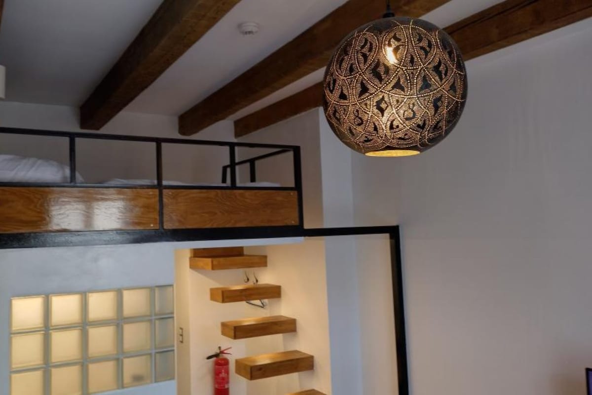Une pièce avec un lit en mezzanine, un luminaire suspendu et des étagères intégrées.