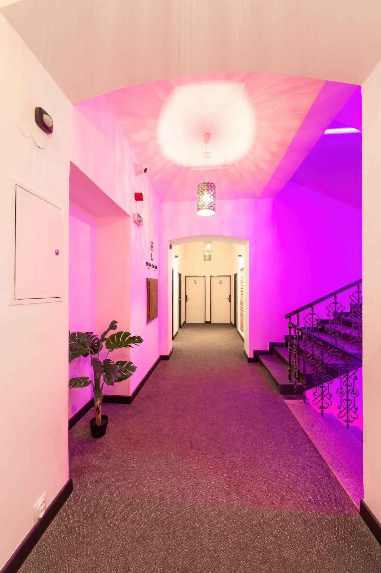 A hallway with a carpeted floor, a potted plant, a staircase with ornate railings, and a ceiling light fixture.