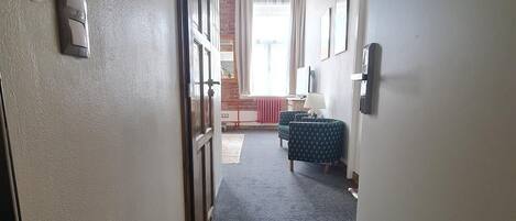 A hallway with a carpeted floor, a door on the left, and a window at the end.