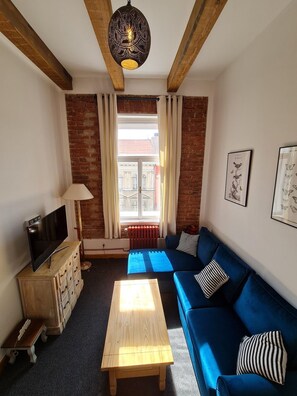 Una habitación amoblada con sofá, mesa de centro, televisión, lámpara y ventana con cortinas.