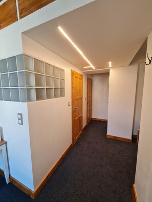 Un pasillo con suelo alfombrado, puertas de madera y una pared con paneles de vidrio esmerilado.