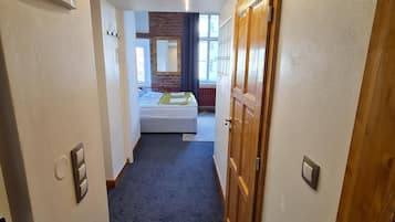 Ein schmaler Flur führt zu einem Schlafzimmer mit einem Bett, einem Spiegel und einem Fenster.