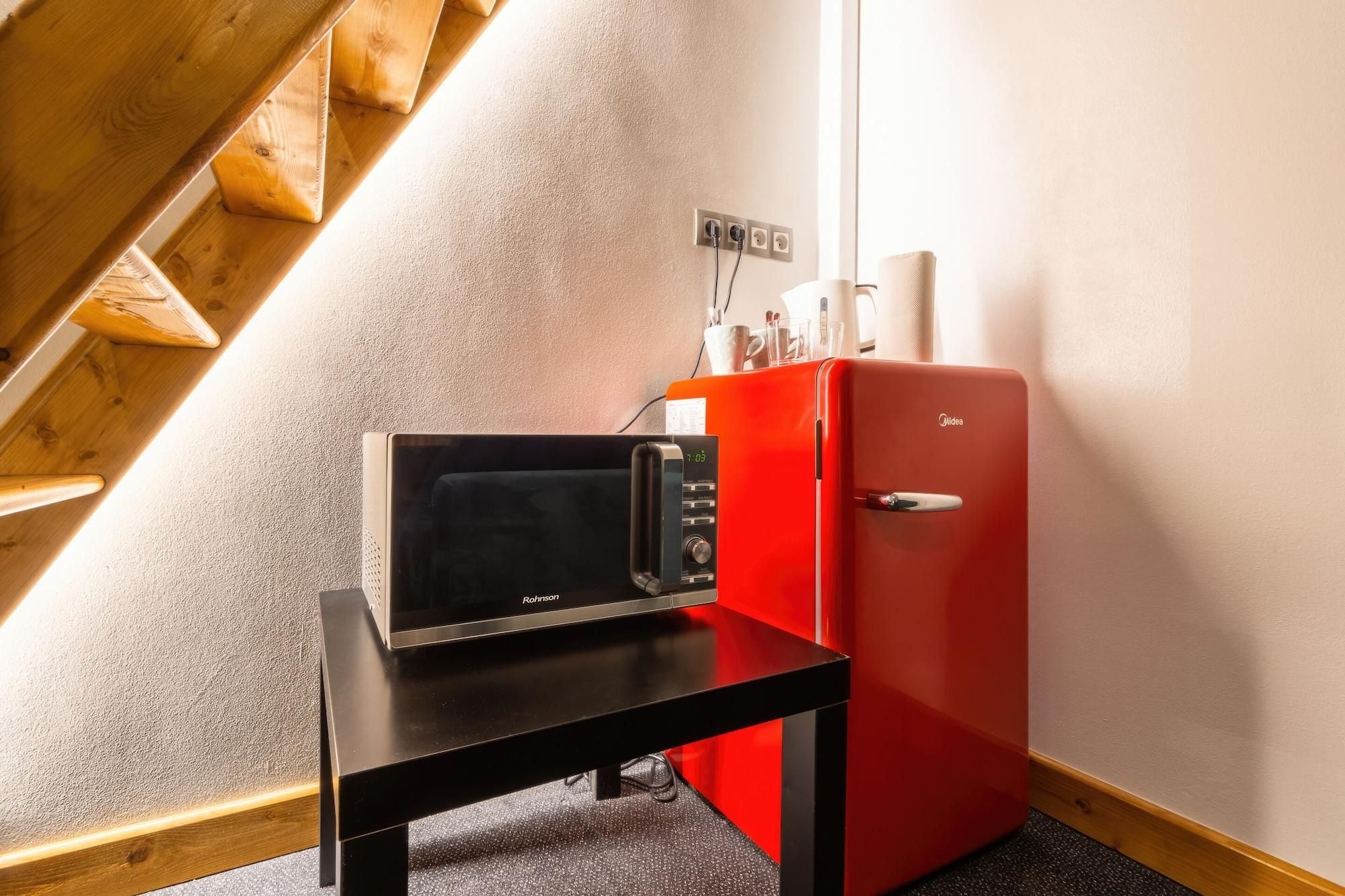 Una kitchenette con microondas, un refrigerador rojo y una mesa de madera.